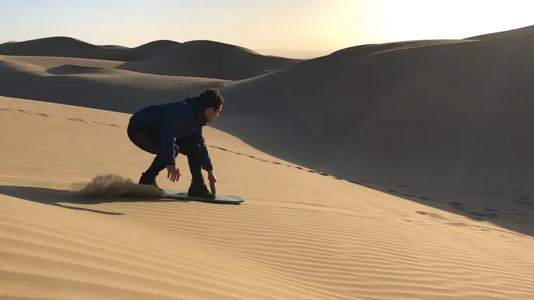 Gabriel sandboarding down a dune at sunset